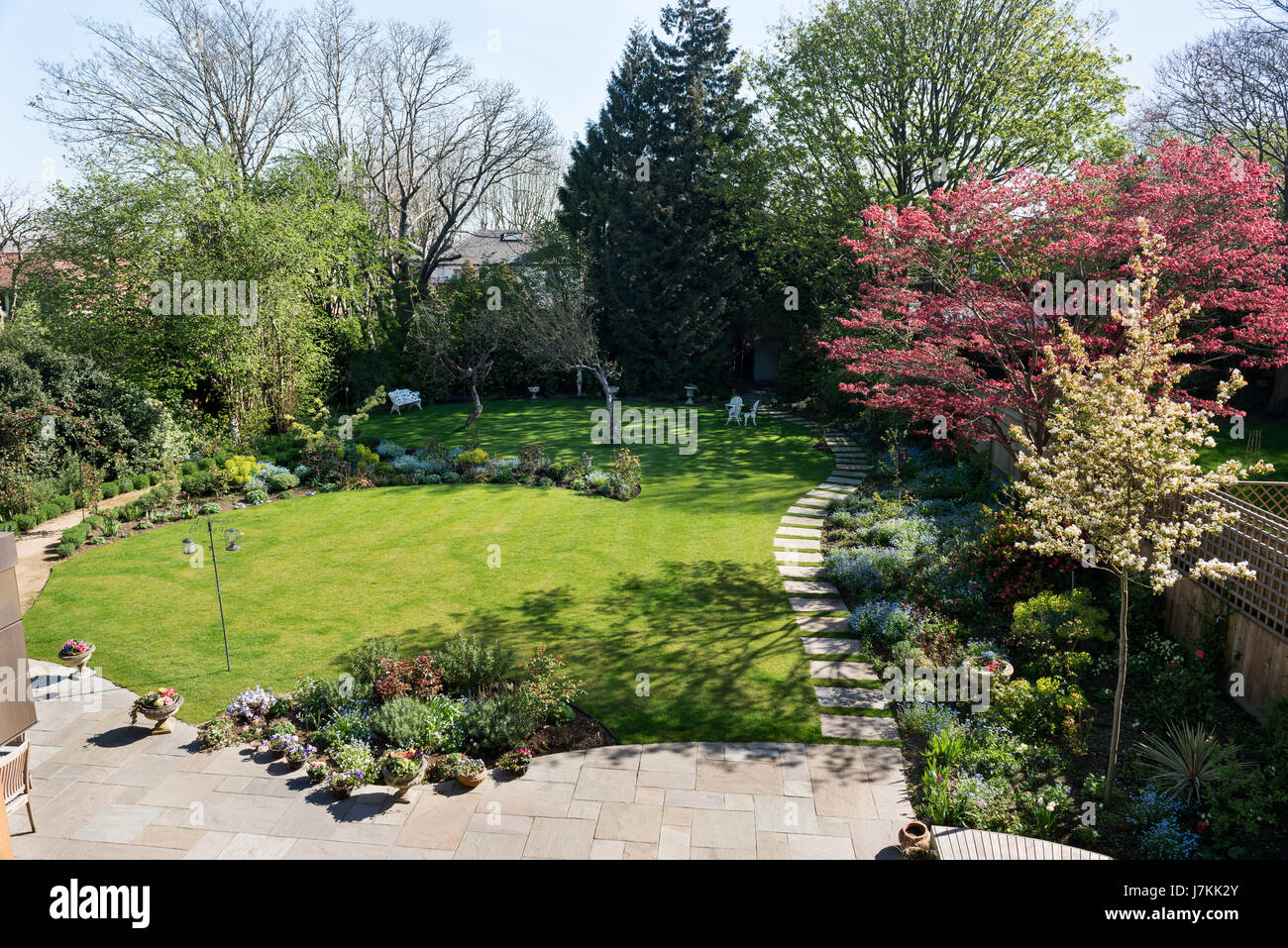 Suburban garden with paved walkway, lawn and assorted planting schemes. Stock Photo