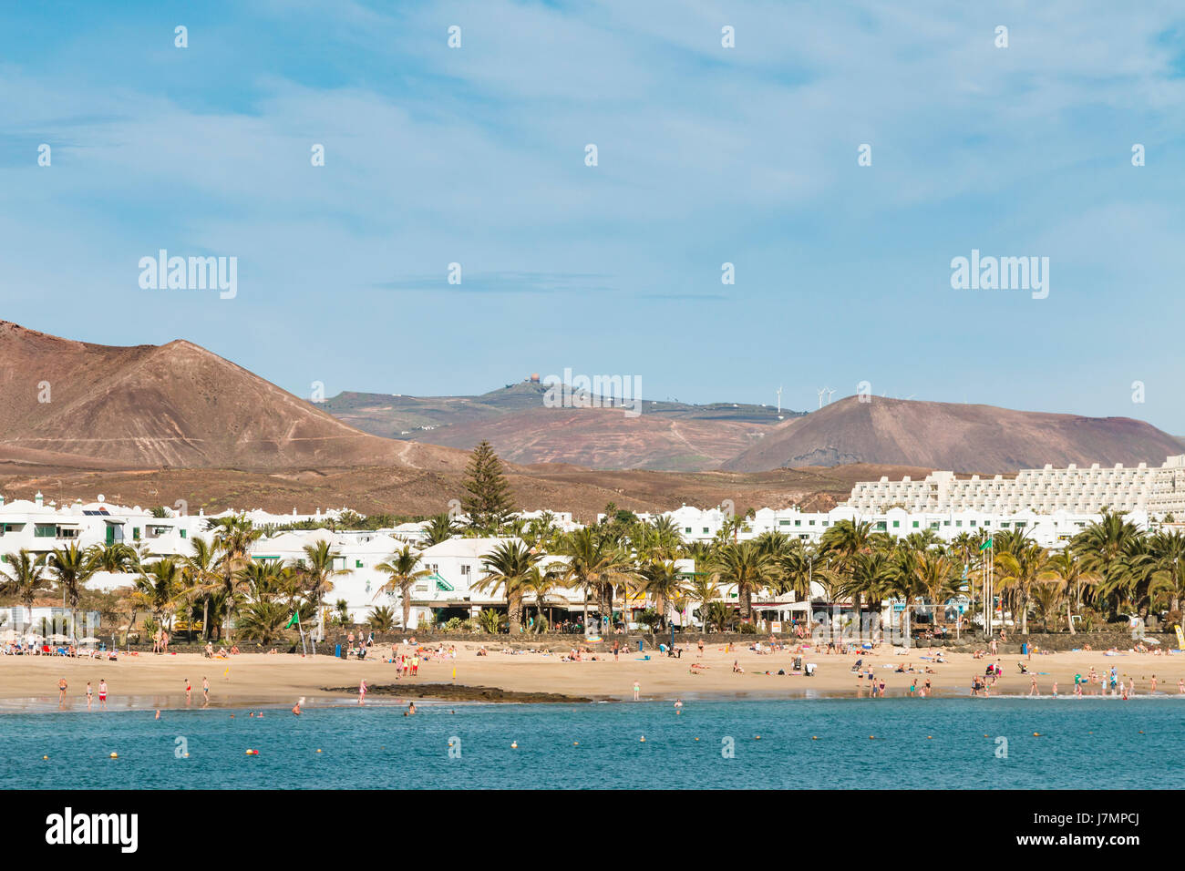 LANZAROTE - JANUARY 14: People at Costa Teguise Beach in Lanzarote, Spain with the village in the background on January 14, 2016. Stock Photo