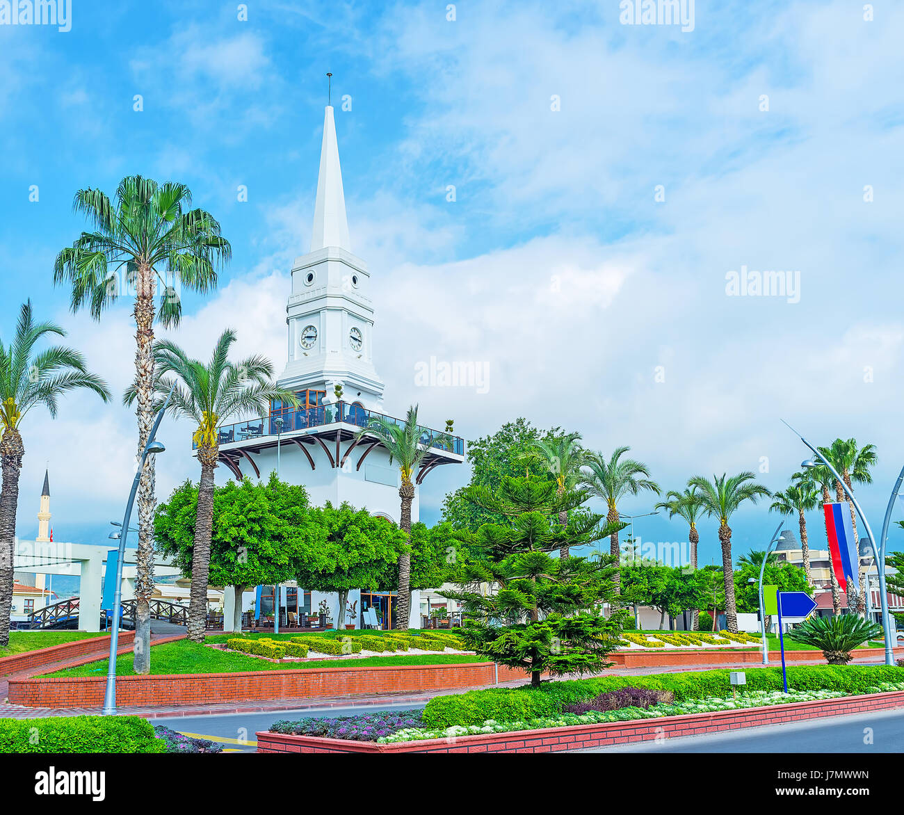 The lush greenery of Ataturk boulevard hides the white Clock tower, rising over the trees, Kemer, Turkey. Stock Photo