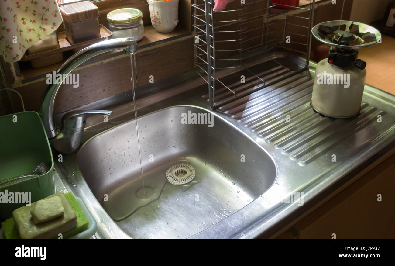 A faucet flowing water on a kitchen sink with a camping stove, contemporary still life. Stock Photo