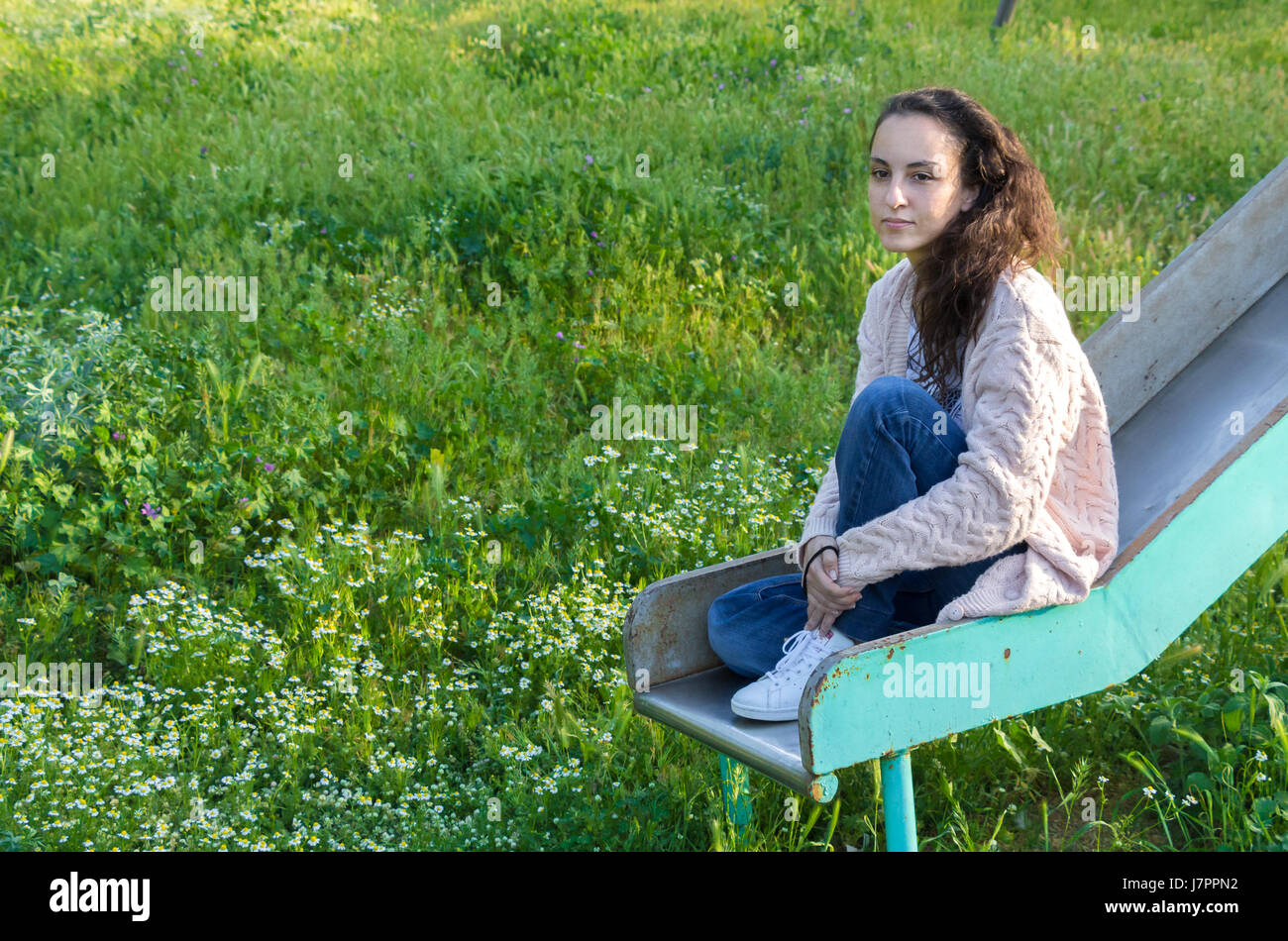 Portrait of a young woman looking away sitting on a slide at a park, thinking. Stock Photo