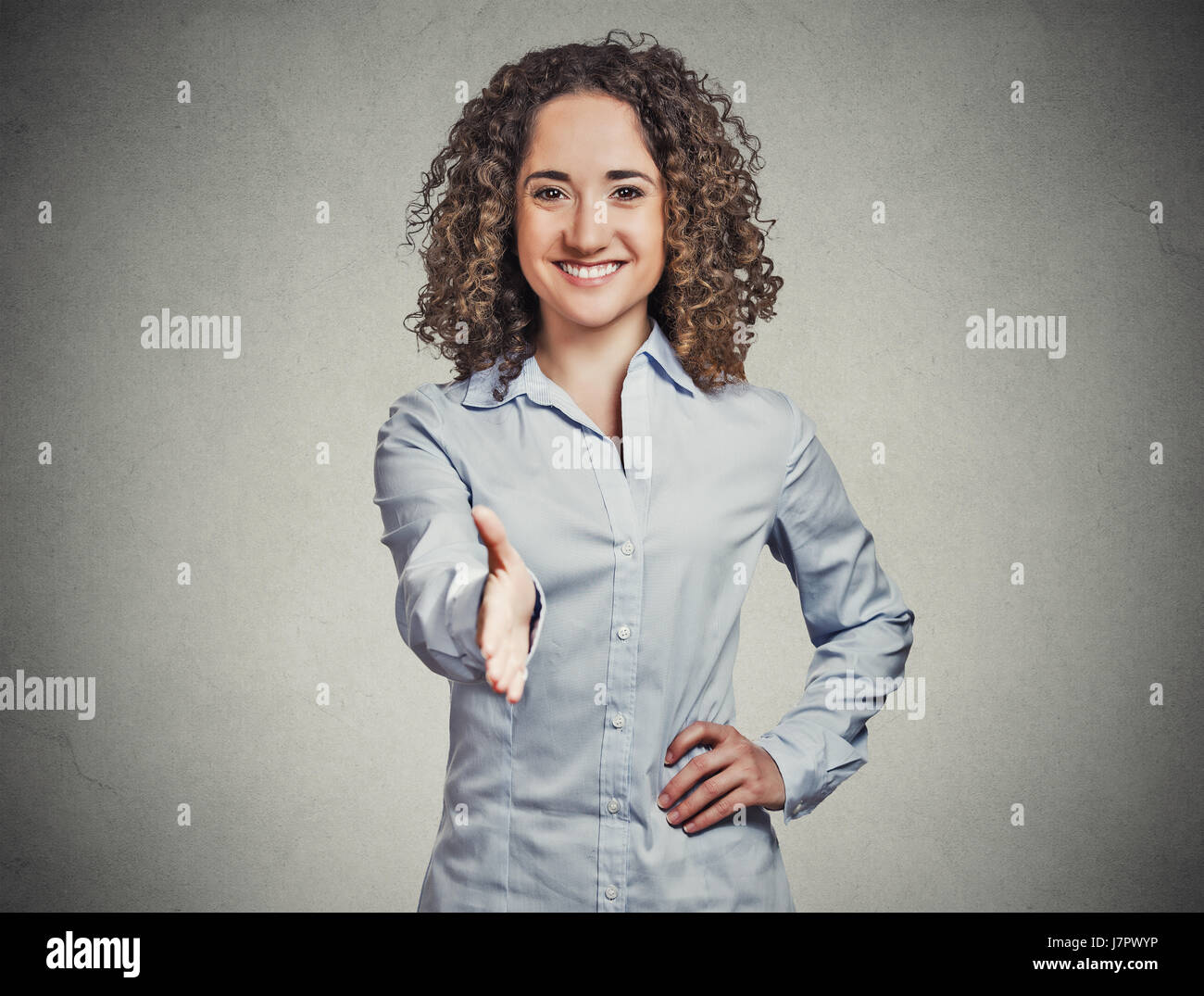 Closeup portrait, young, curly, brown hair, smiling woman, student, customer service agent giving you handshake isolated grey wall background. Positiv Stock Photo
