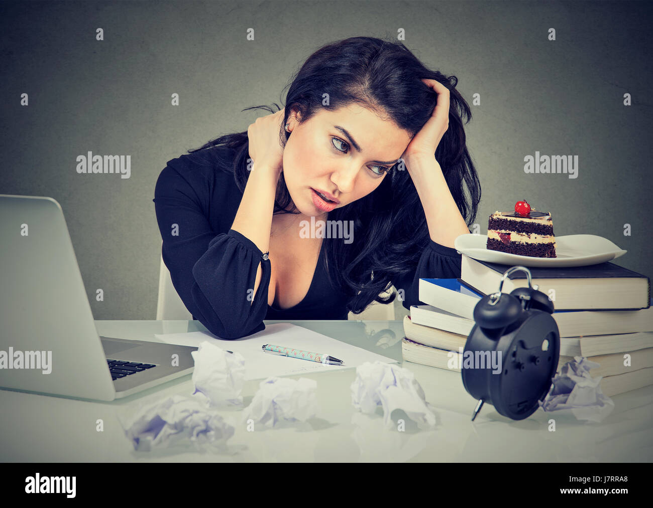 stressed woman sitting at desk in her office overworked craving sweet cake Stock Photo