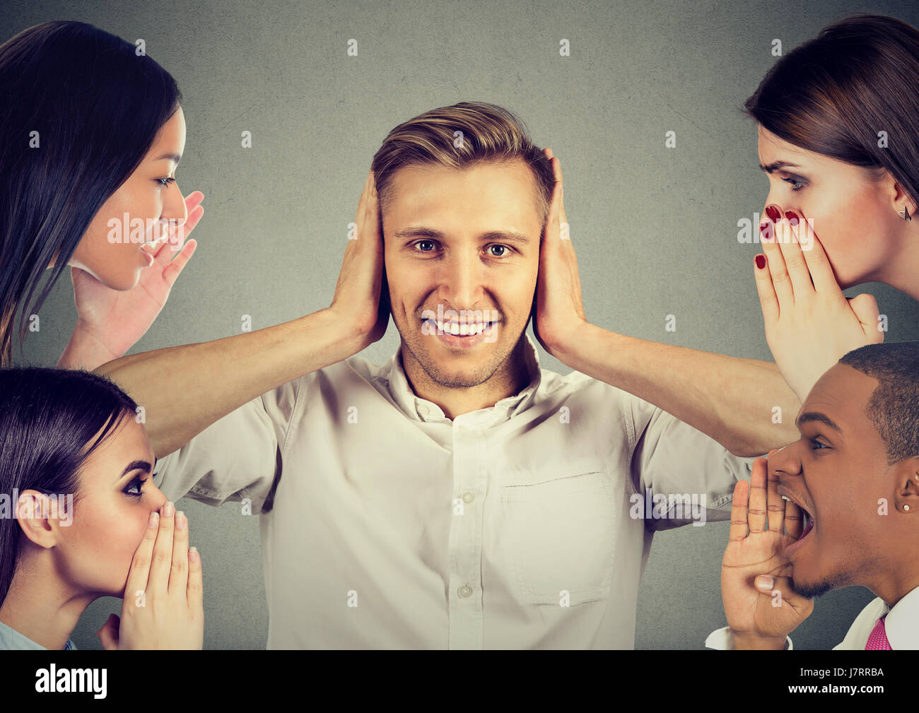 Man and women whispering a secret latest gossip to a happy young man who covers ears and ignoring all surrounding noise Stock Photo