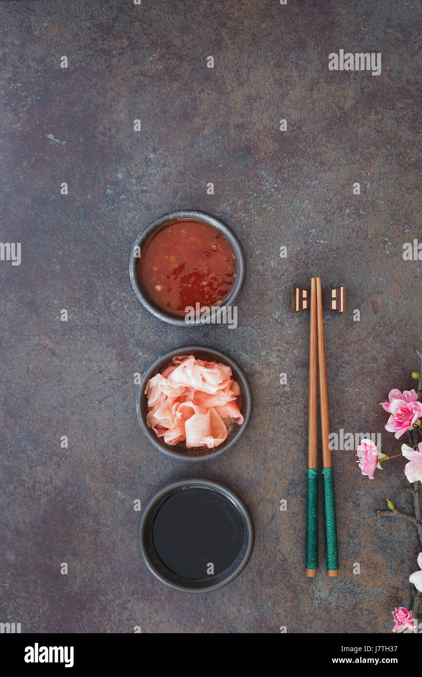 Sushi Set. Japanese sushi chopsticks,  soy and chili sauce bowl and pickled ginger on dark stone background Stock Photo