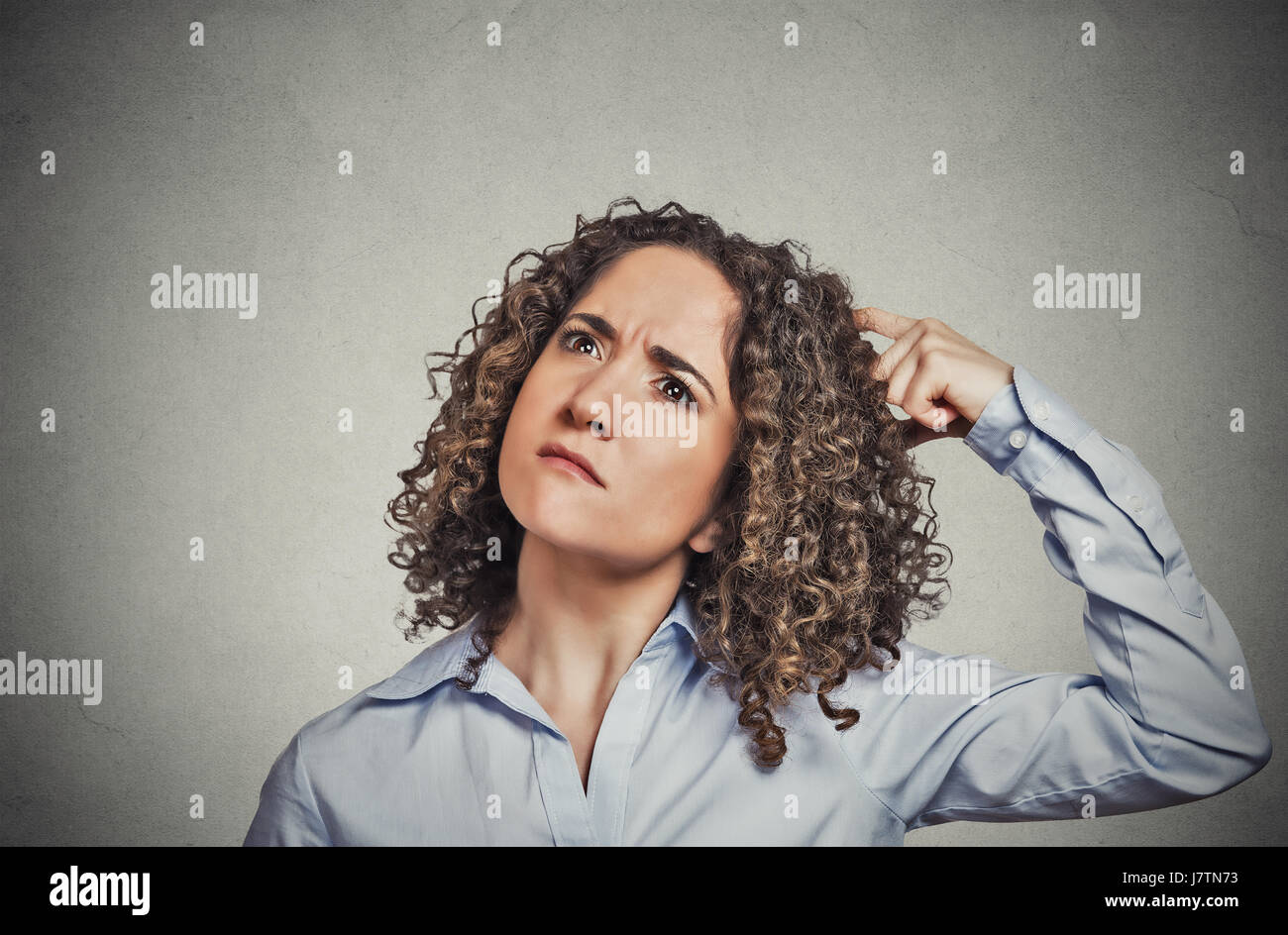Closeup portrait young woman scratching head, thinking daydreaming about something wondering looking up isolated on grey wall background. Human facial Stock Photo