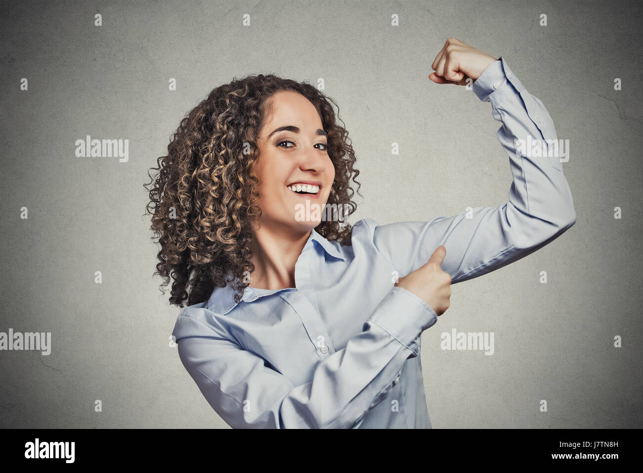 Closeup portrait beautiful fit young healthy model woman flexing muscles showing her strength isolated grey wall background. Positive emotion facial e Stock Photo