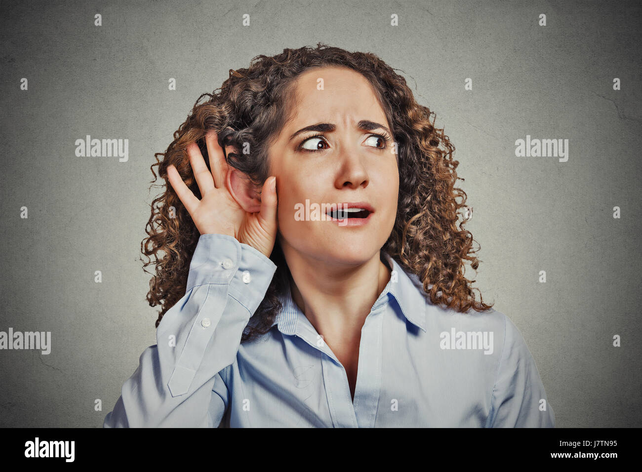 Closeup portrait surprised young nosy woman hand to ear gesture carefully intently secretly listening juicy gossip conversation news privacy violation Stock Photo