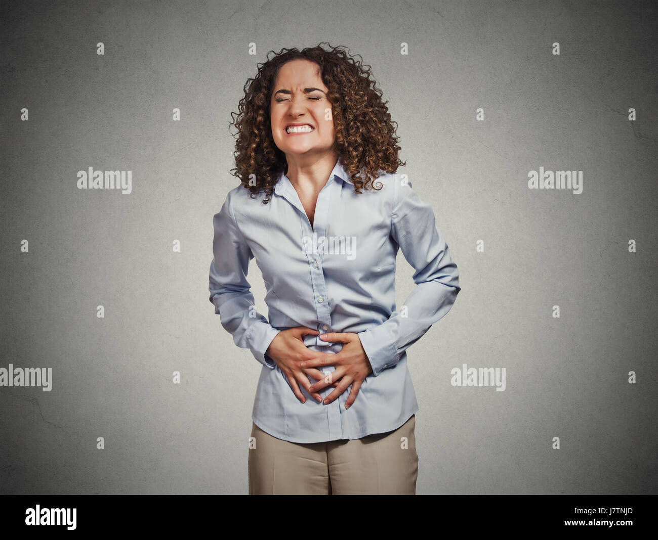 Portrait young woman hands on stomach having bad aches pain isolated grey wall background. Food poisoning, influenza, cramps. Negative emotion facial  Stock Photo