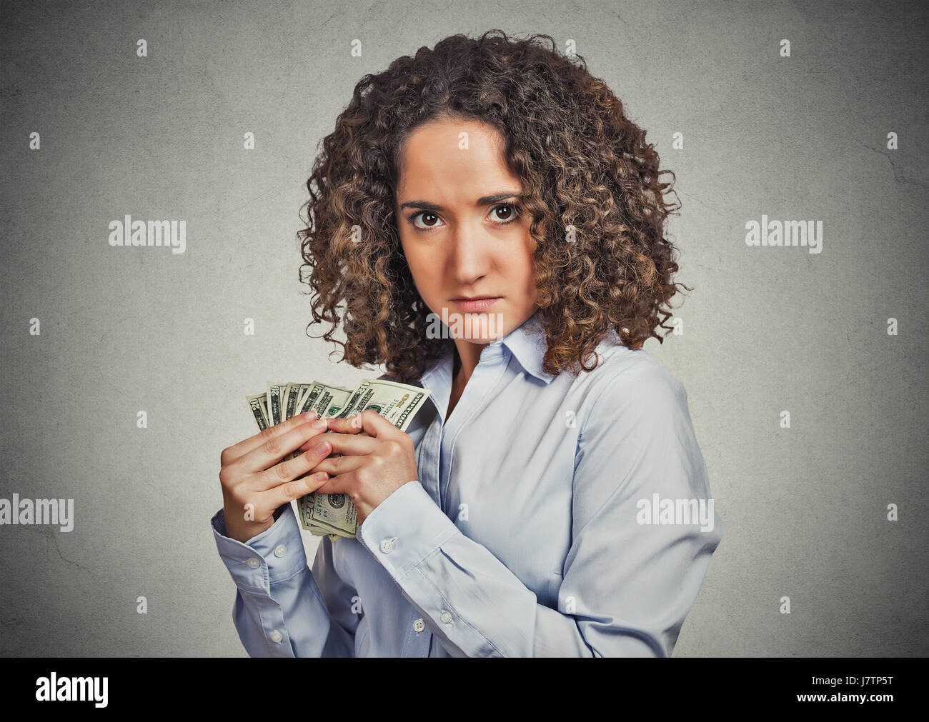 Closeup portrait greedy young woman corporate business employee, worker, student holding dollar banknotes tightly isolated grey wall background. Negat Stock Photo