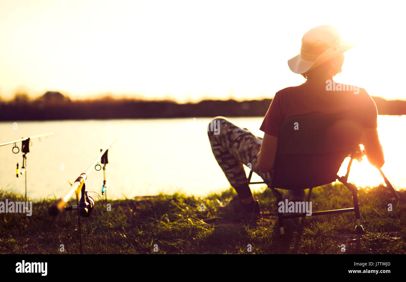 Young man fishing on lake at sunset enjoying hobby Stock Photo