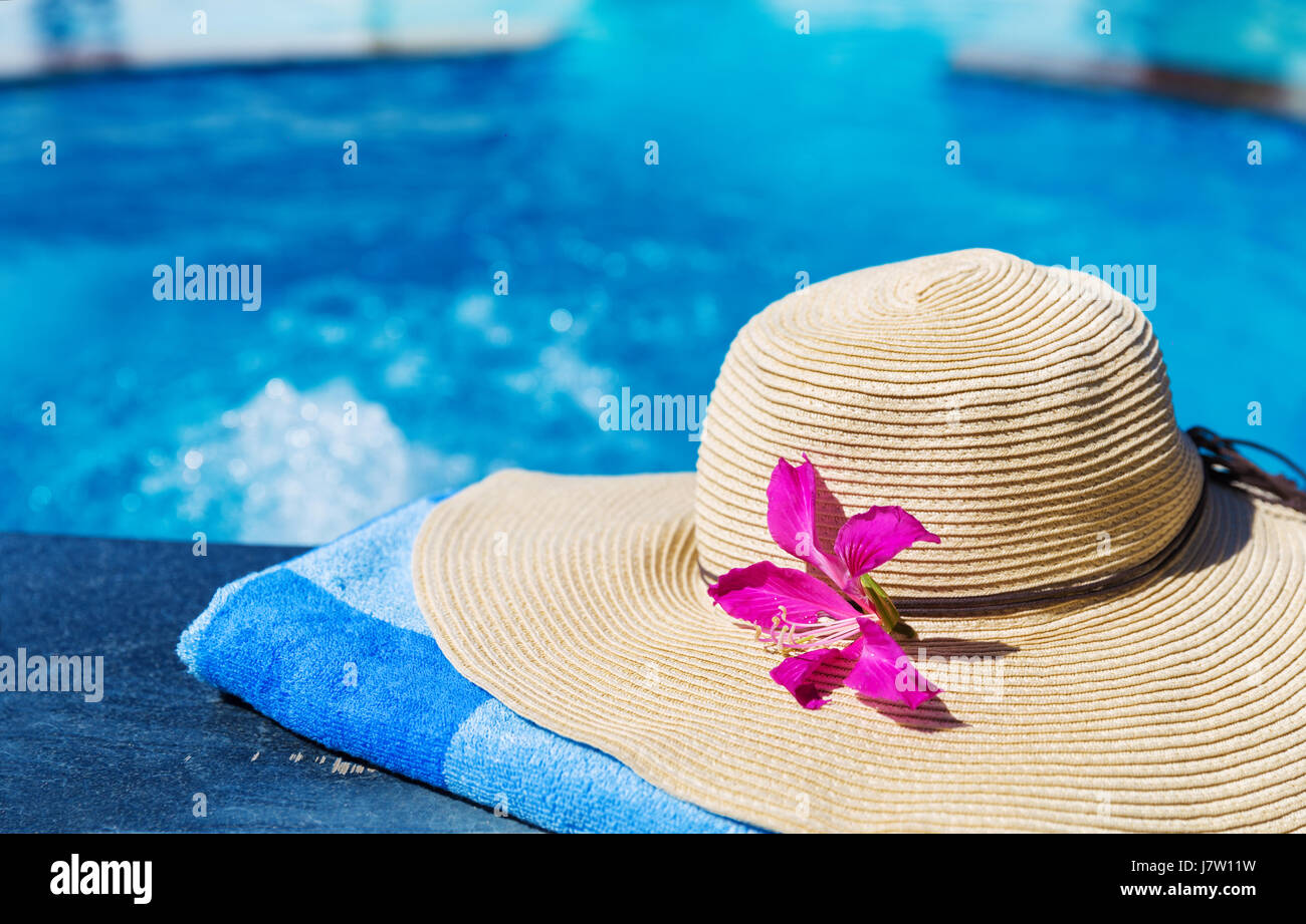 Straw hat with orchid flower and blue towel near swimming pool ...