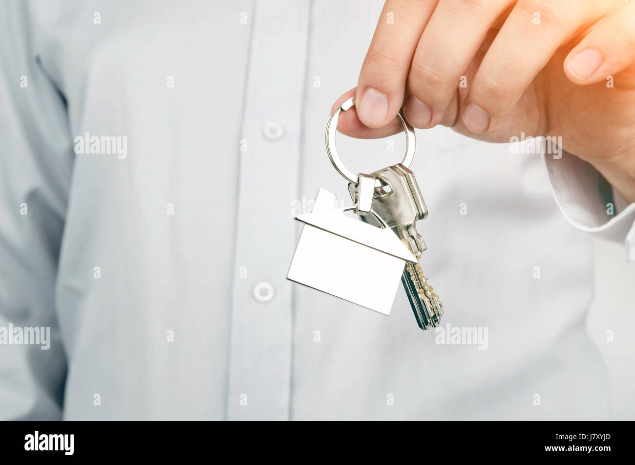 Estate agent holding keys to new house. Home shape chrome pendant Stock Photo