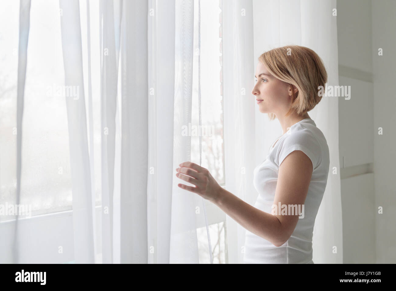 Young woman wearing white t-shirt looking out through window Stock Photo