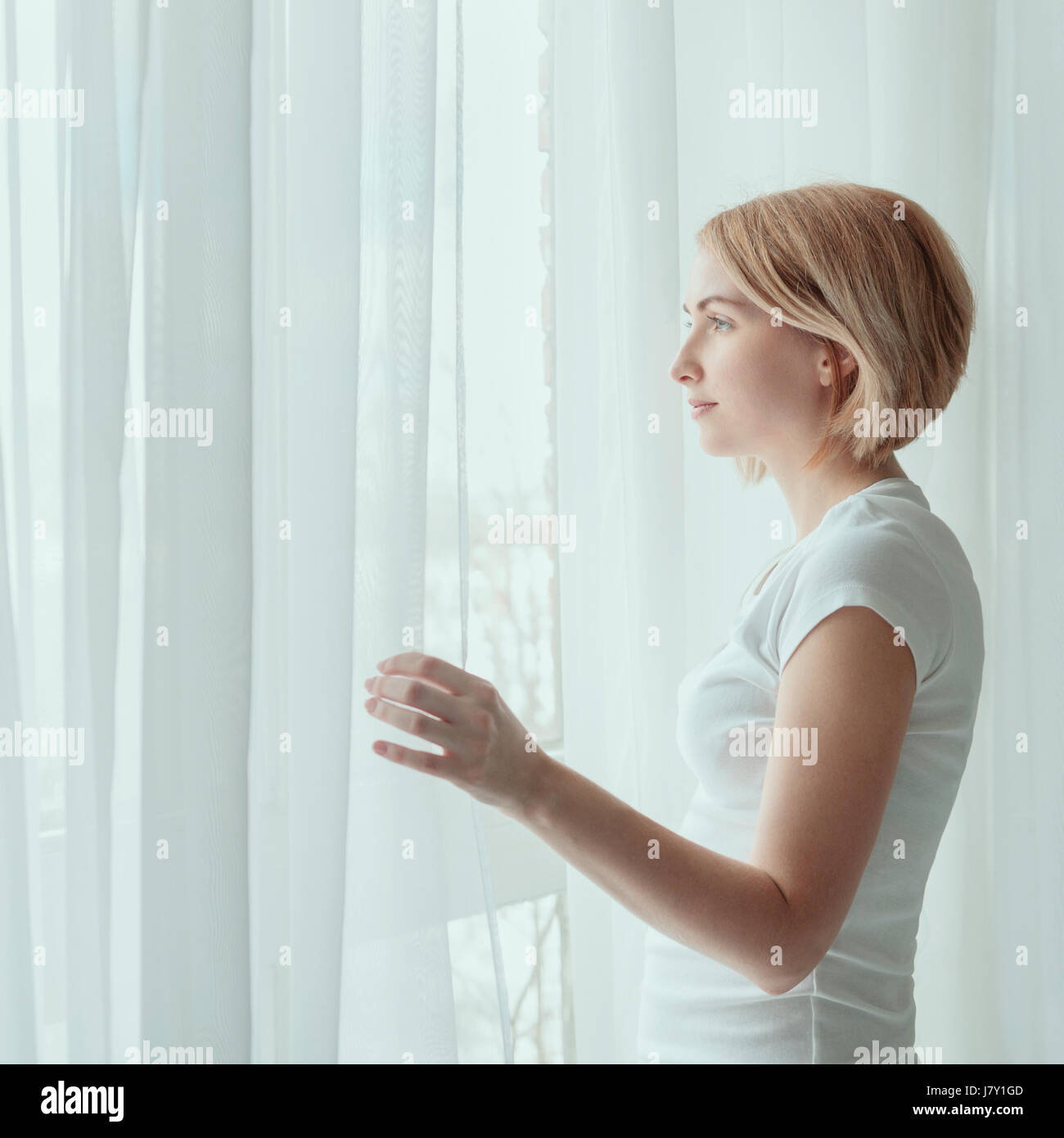 Young woman wearing white t-shirt looking out through window Stock Photo