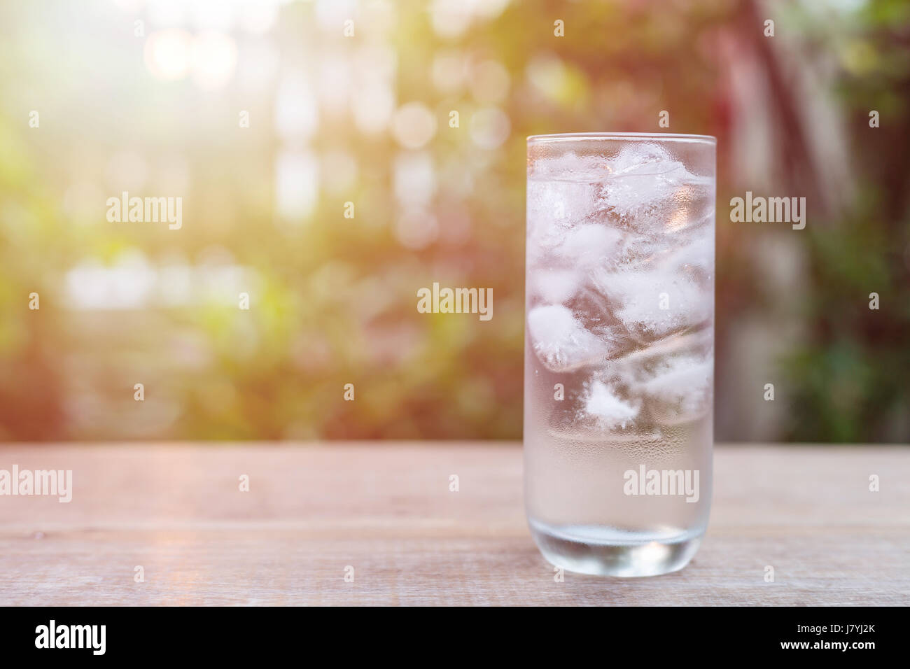 Close up glass of cold water with ice on table with blur nature garden background Stock Photo