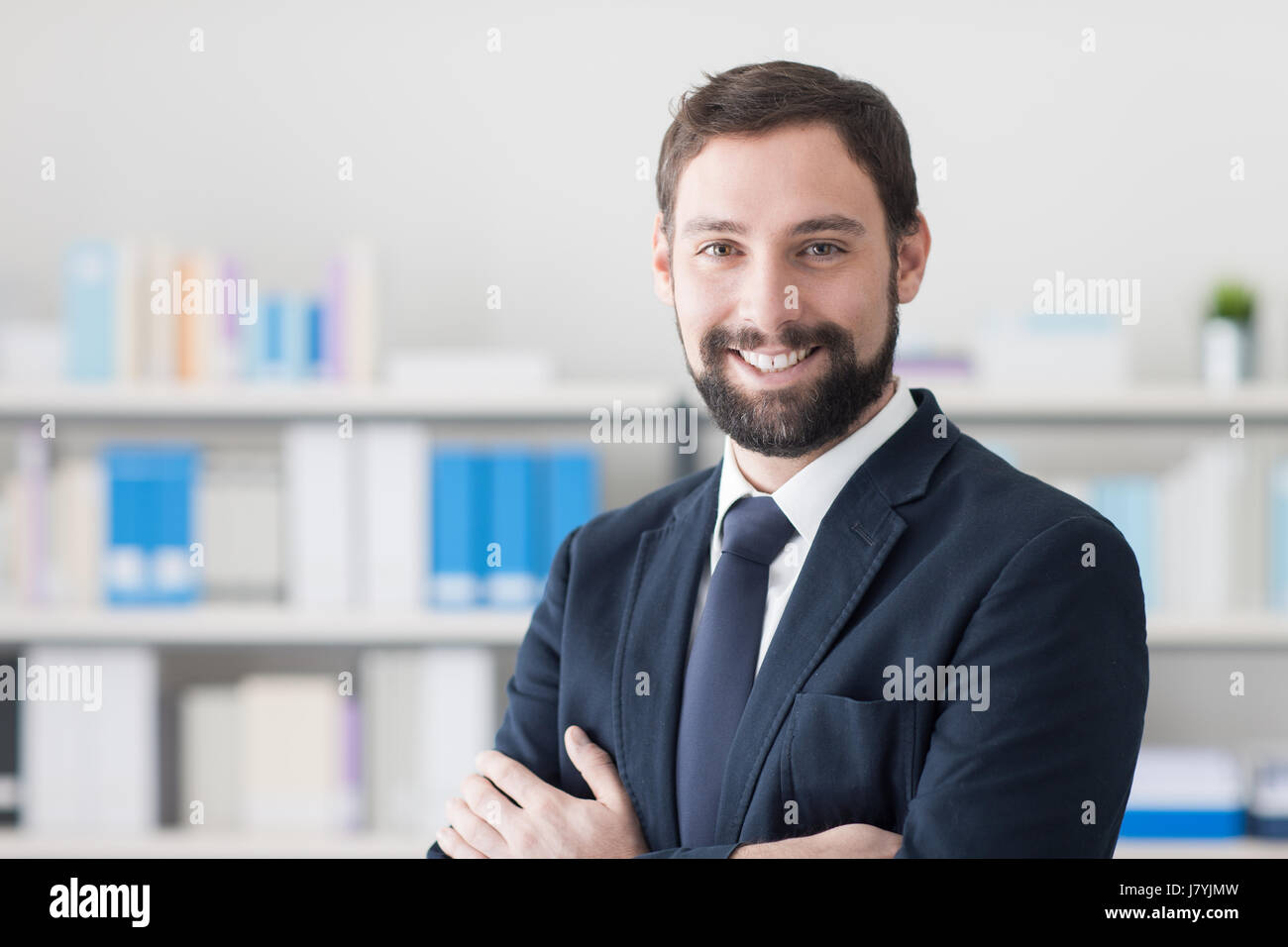 Confident young businessman posing in his office and smiling at camera ...