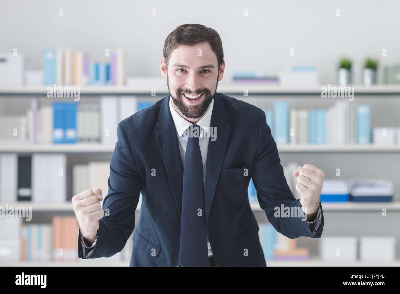 Cheerful successful businessman smiling in his office with raised fists, winning and enthusiasm concept Stock Photo