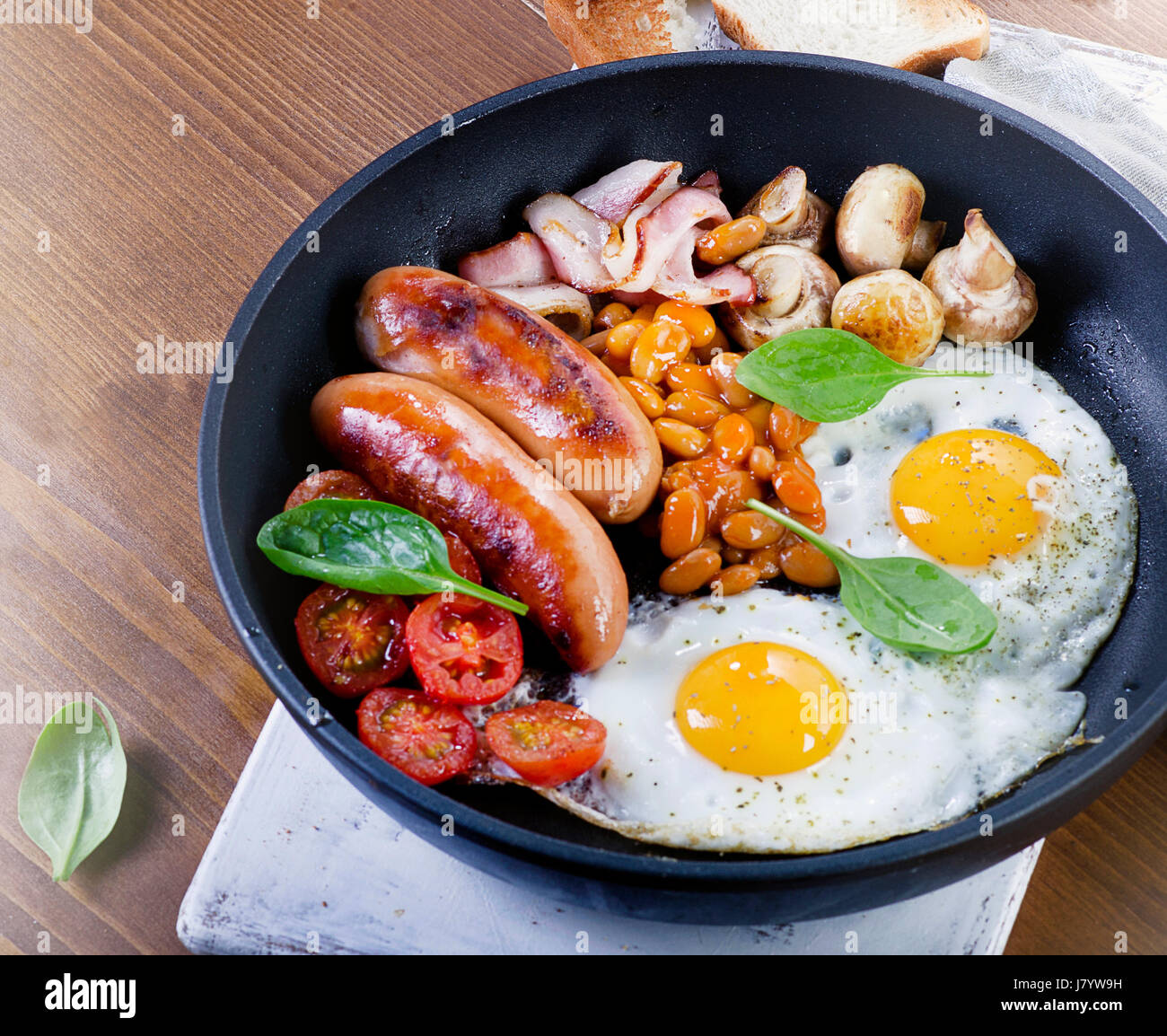 Full English breakfast in pan with fried eggs, sausages, bacon, beans