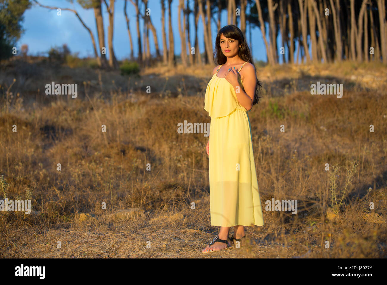 Serious young woman wearing a yellow summer dress standing outdoors ...