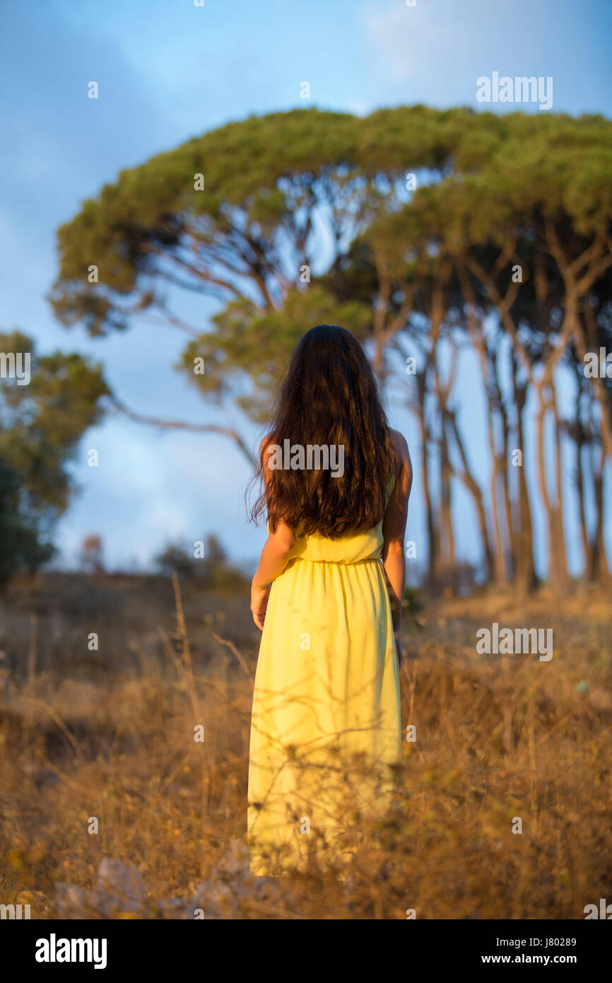 Rear view of a young woman wearing a yellow summer dress standing ...