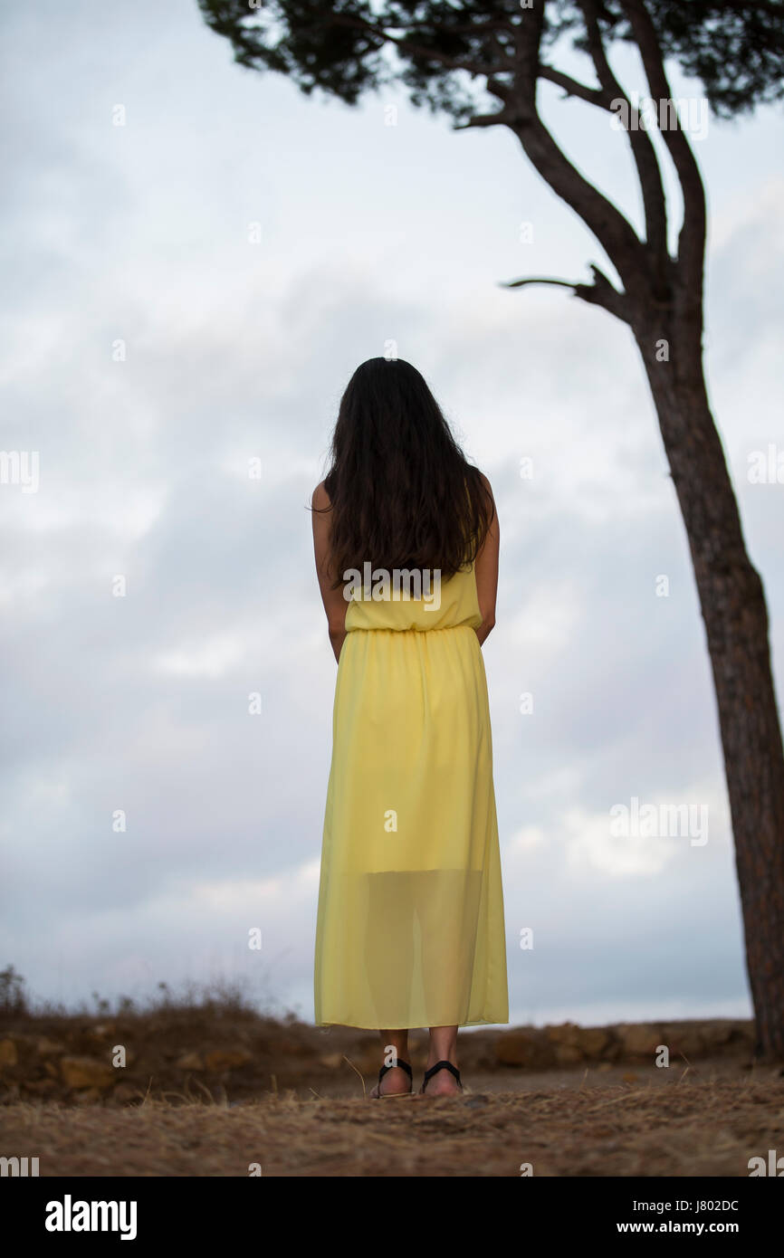 Woman in yellow summer dress standing next to a tree Stock Photo - Alamy