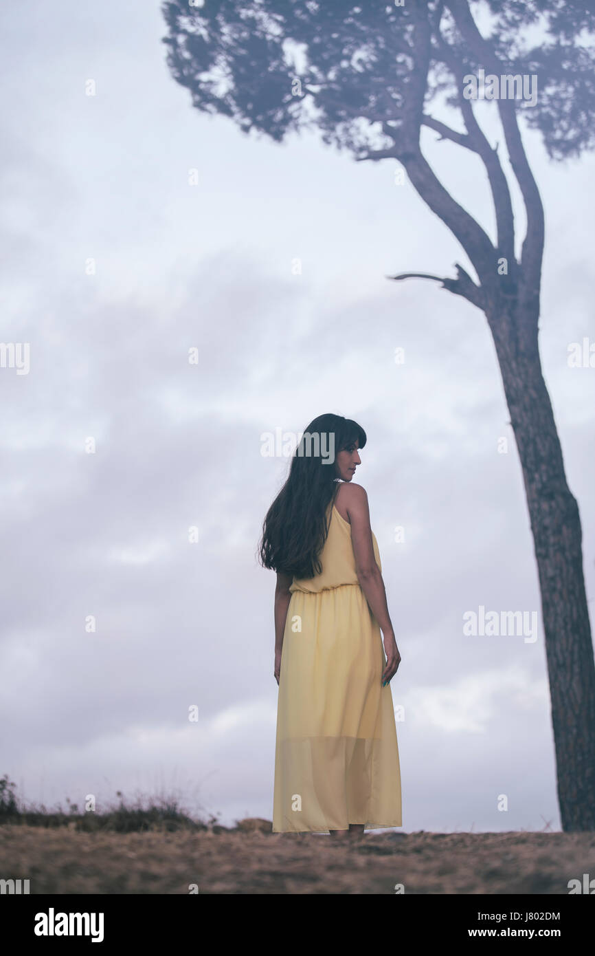 Woman in yellow summer dress standing next to a tree Stock Photo - Alamy