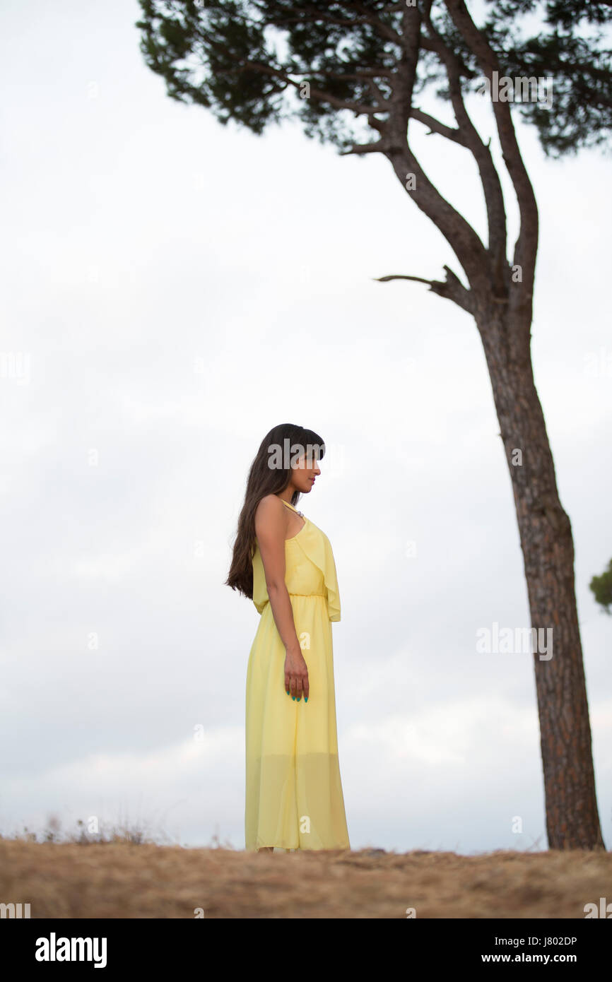 Woman in yellow summer dress standing next to a tree Stock Photo - Alamy