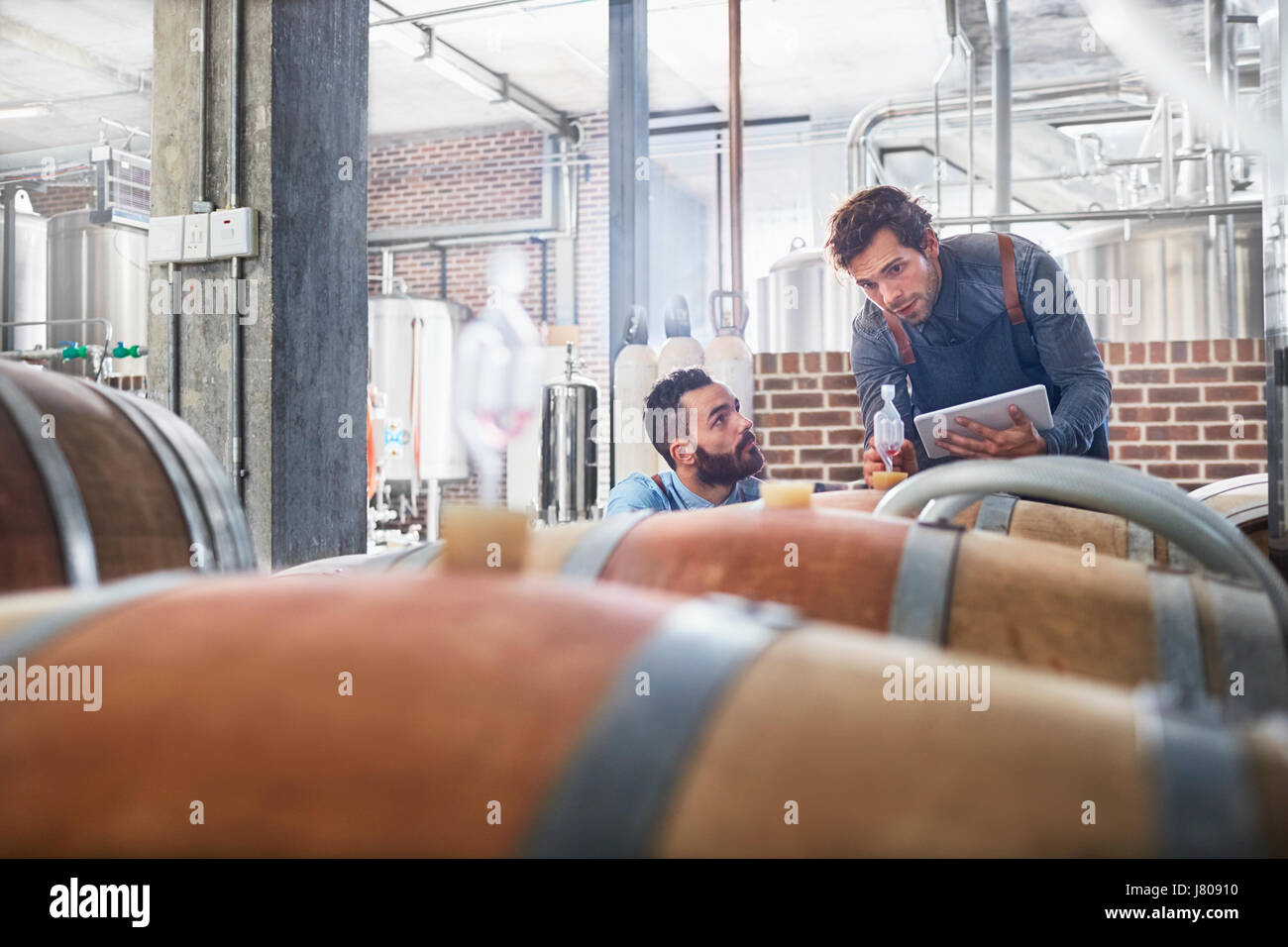 Male winemakers with digital tablet checking wood casks Stock Photo