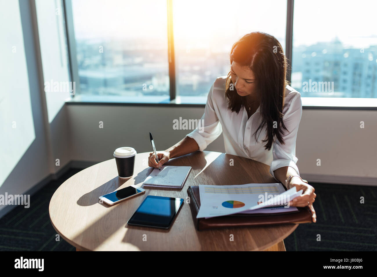 Young woman entrepreneur making business working at coffee table in office. Female business executive making business plans with a coffee cup on her t Stock Photo