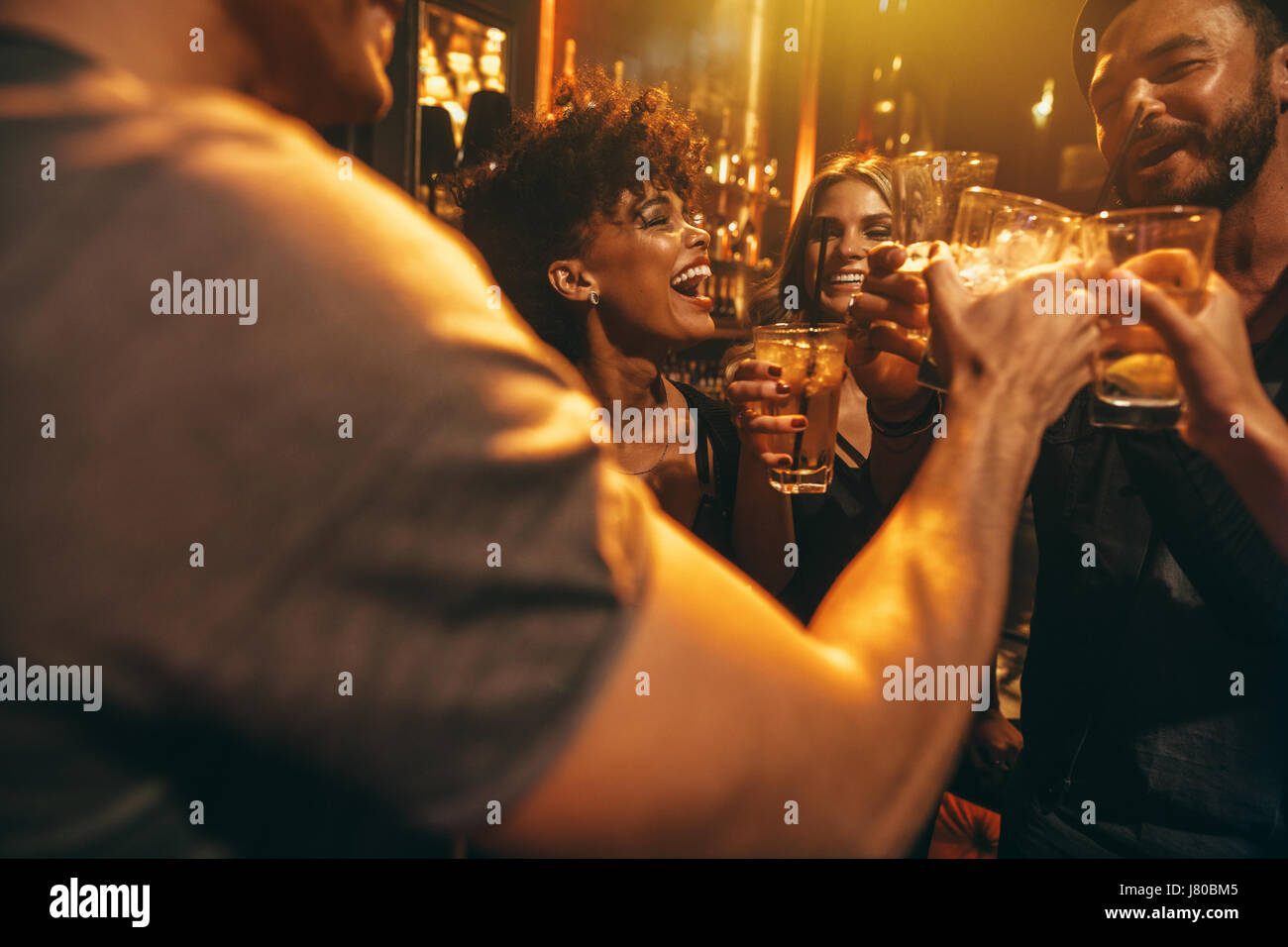 Happy group of people enjoying drinks at bar. Young friends at nightclub toasting cocktails. Stock Photo