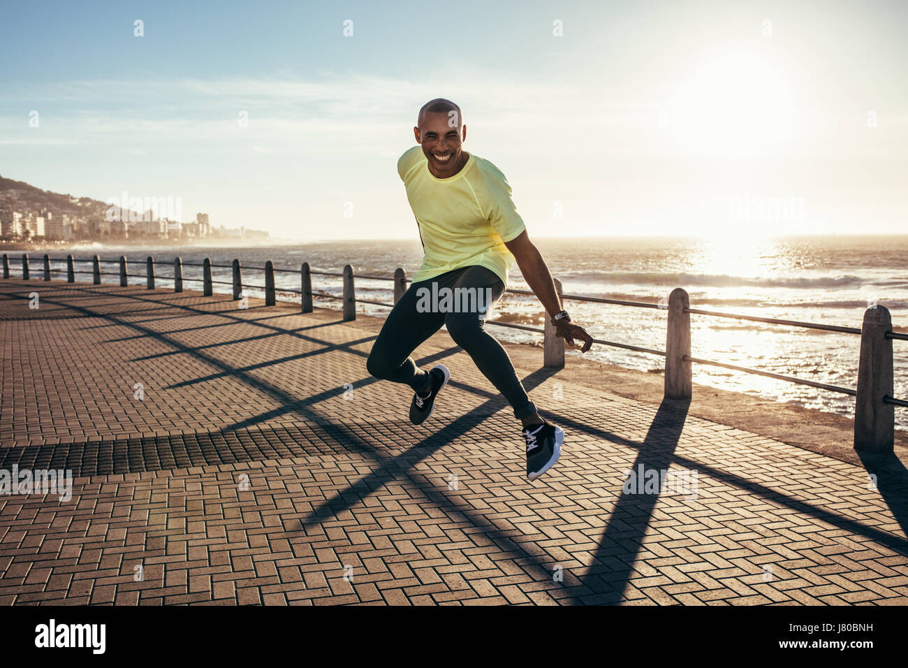 Young african man jumping on a road by the sea. Excited young runner jumping. Stock Photo