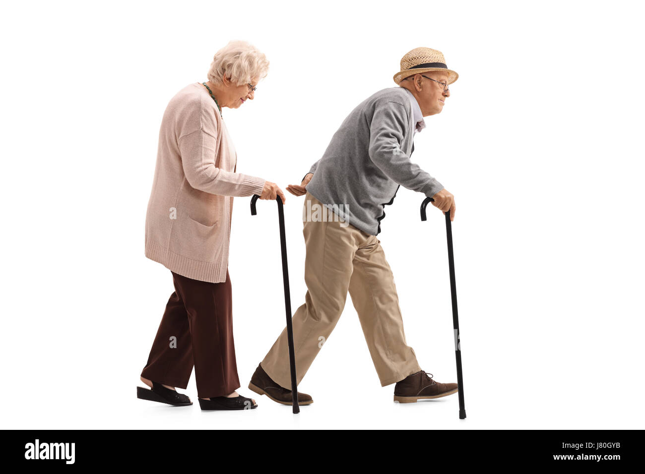 Full length profile shot of an elderly man and an elderly woman with canes walking isolated on white background Stock Photo