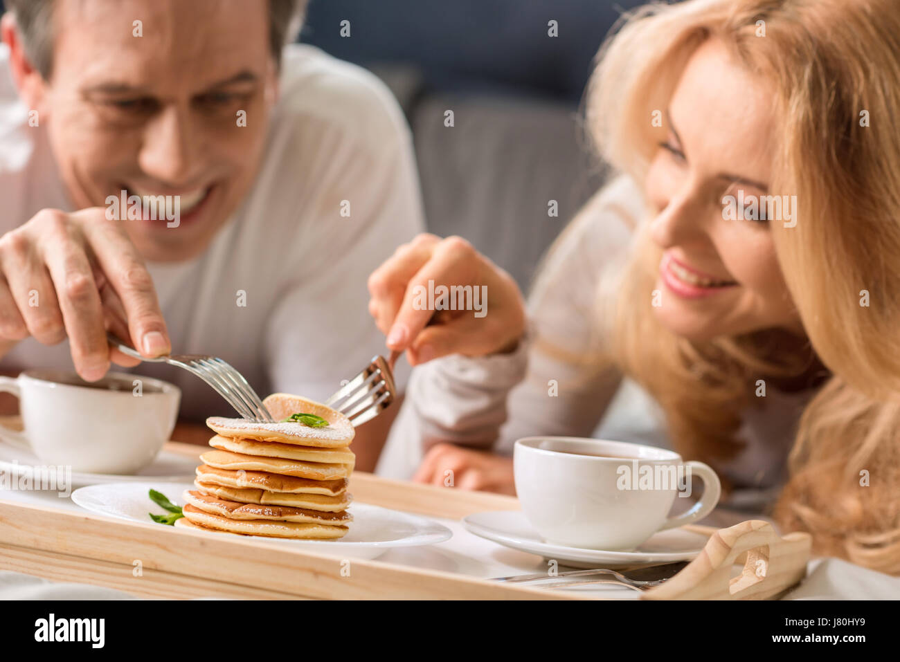 Happy middle aged couple eating pancakes together in bed Stock Photo