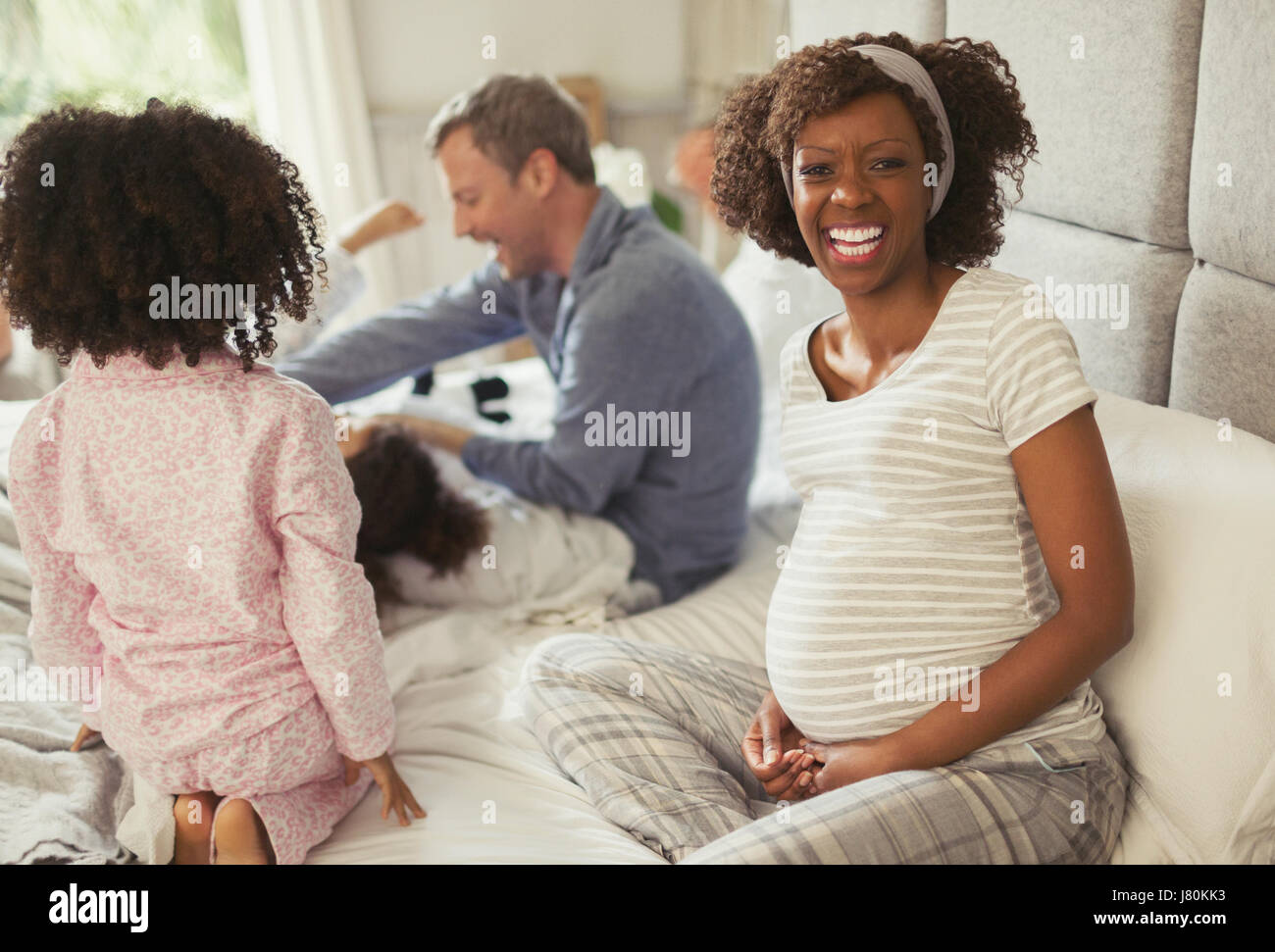 Portrait laughing pregnant woman with young family on bed Stock Photo