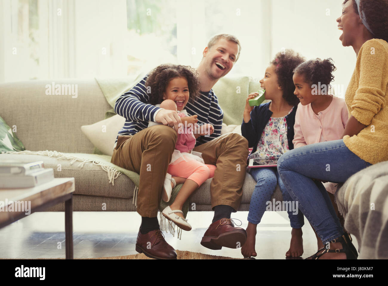 Multi-ethnic young family laughing on sofa Stock Photo