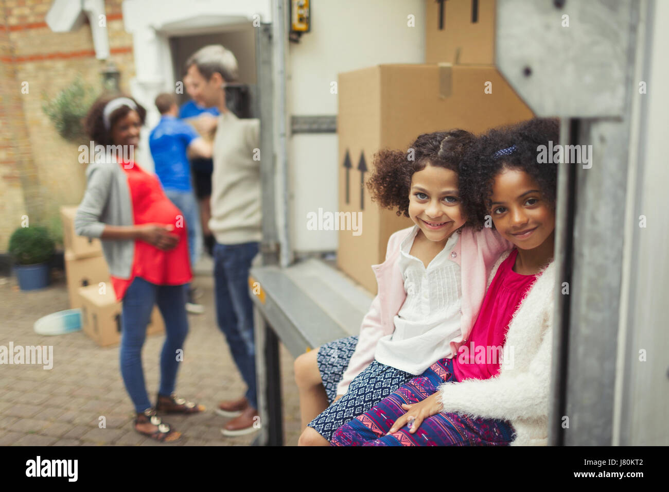 Portrait smiling sisters sitting in moving van outside new house Stock Photo