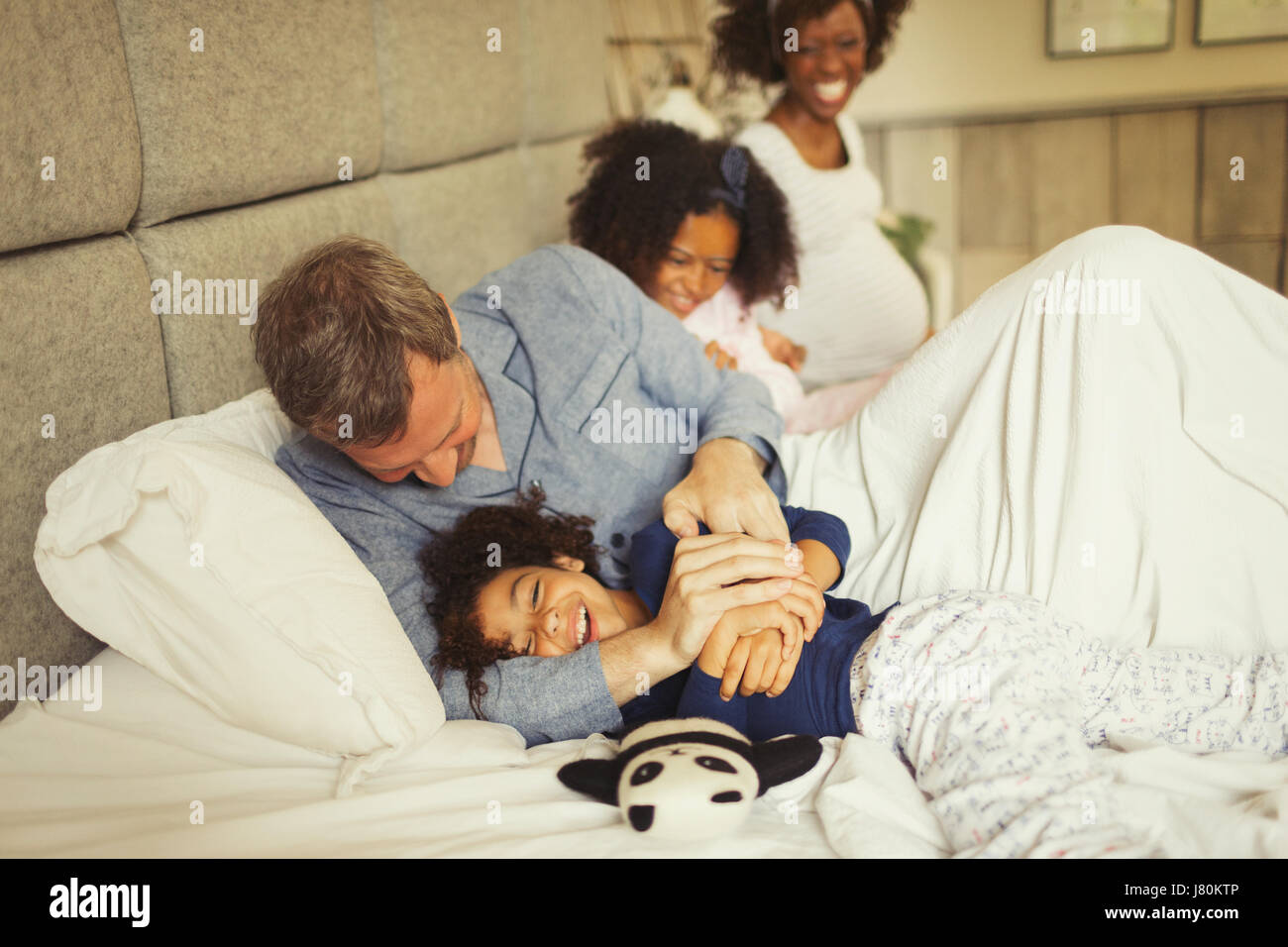 Multi-ethnic father and daughter tickling and laughing on bed Stock Photo