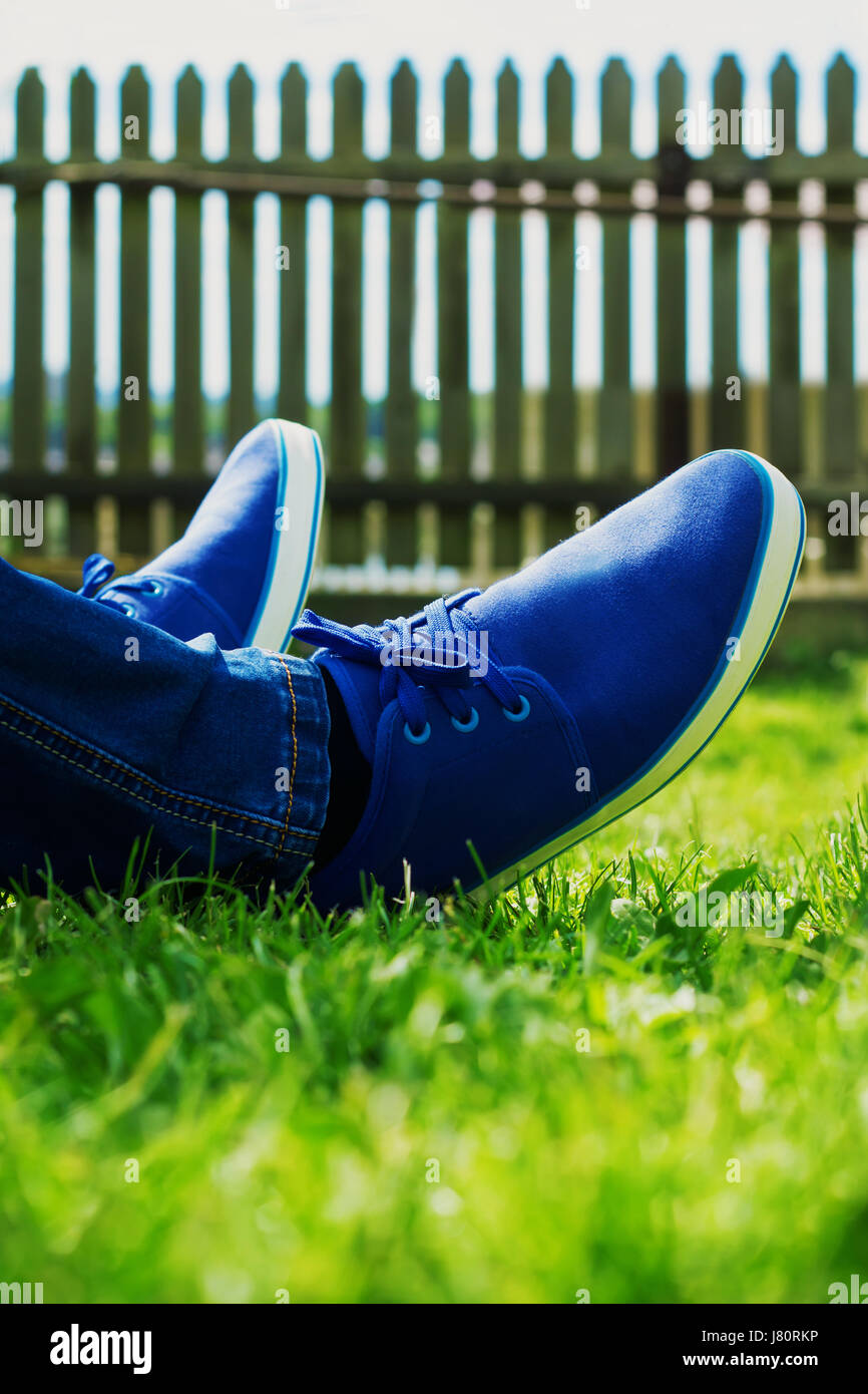 Male feet in blue sneakers lay on a fresh green grass in the backyard. Resting in a sunny summer day. Stock Photo