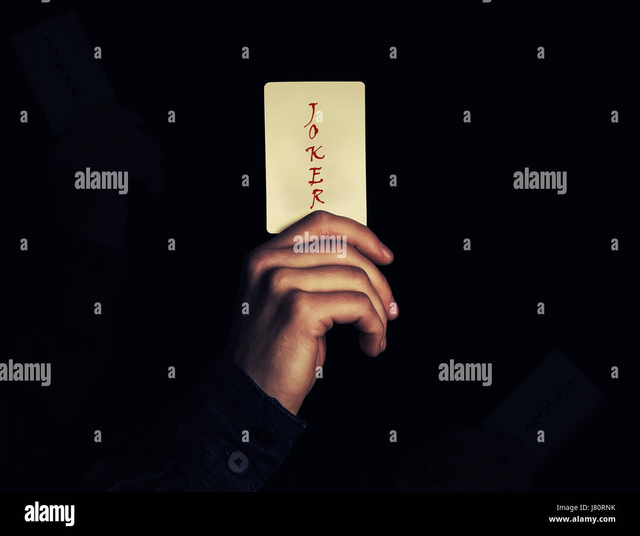 Close up of a man hand holding joker playing card. Illusionist showing a magic trick on a black background. Casino game concept. Stock Photo