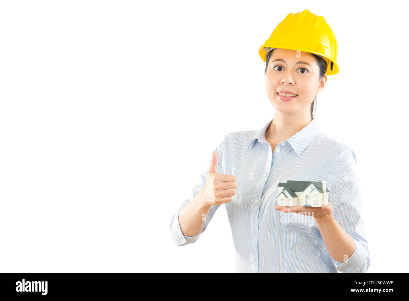 photo of thumbing up young lady architect with holding miniature house model and smiling standing on the blank white background over copyspace wall. C Stock Photo