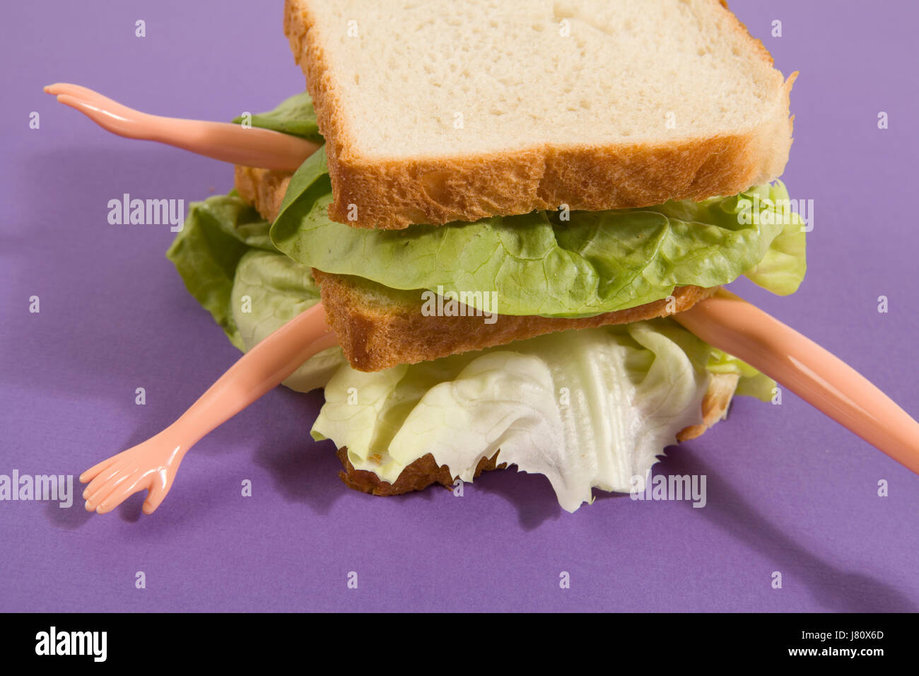 Parts of a doll's body in a sandwich with salad and soft bread on a