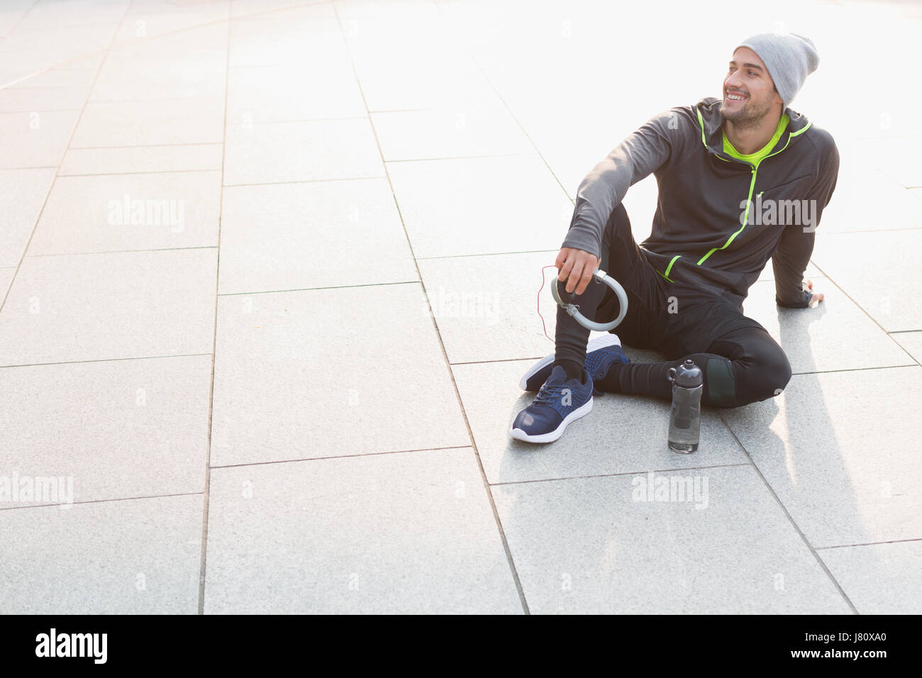 Smiling male runner resting, holding headphones and looking away Stock Photo