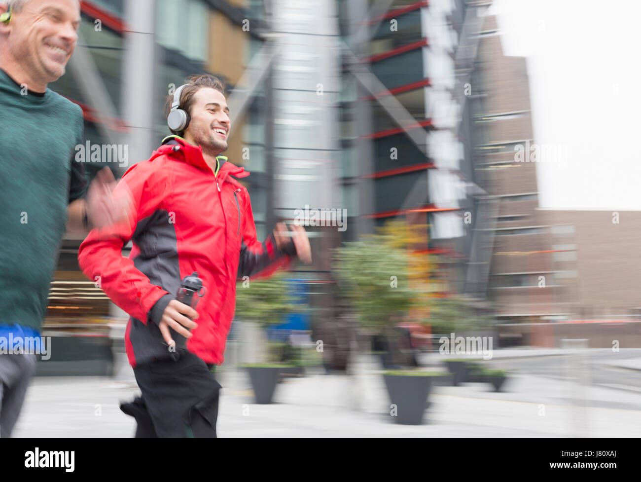 Smiling men running, wearing headphones on urban sidewalk Stock Photo