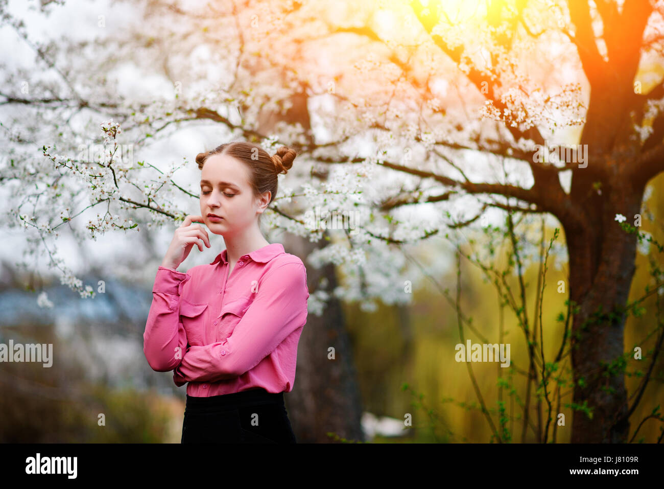 Young beautiful girl in a pink shirt standing under blossoming apple ...