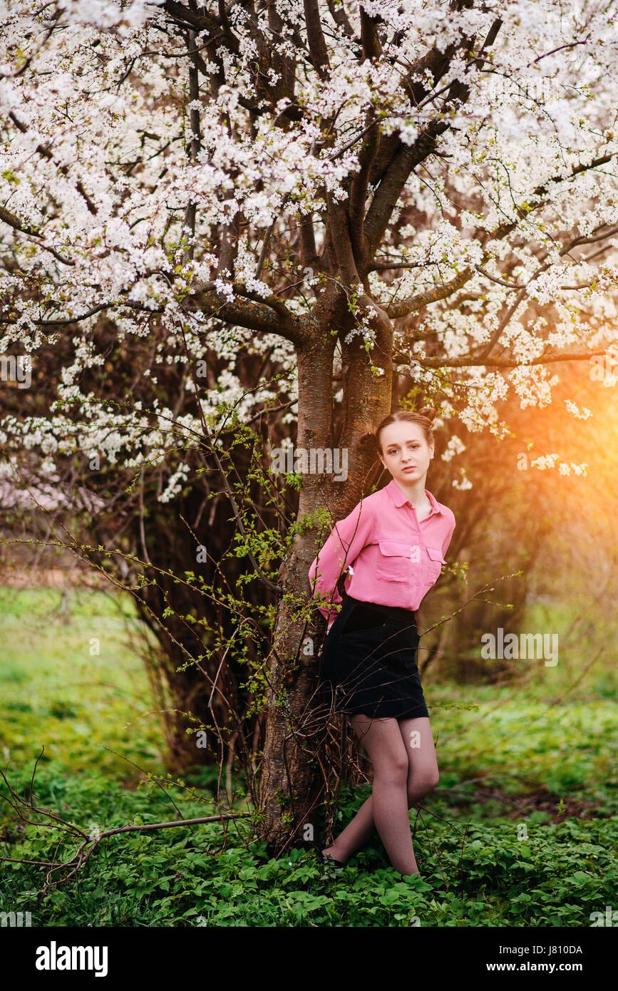Young beautiful girl in a pink shirt standing under blossoming apple ...