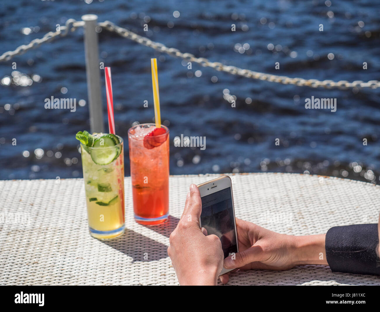 Food blogger photographs with a smartphone two glasses of lemonade on a table on a deck of water background Stock Photo