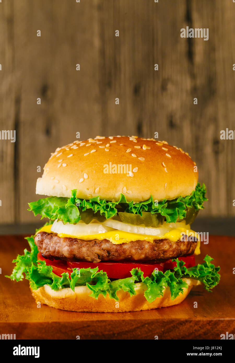 Classic deluxe cheeseburger with lettuce, onions, tomato and pickles on a sesame seed bun. Macro with shallow dof. Stock Photo