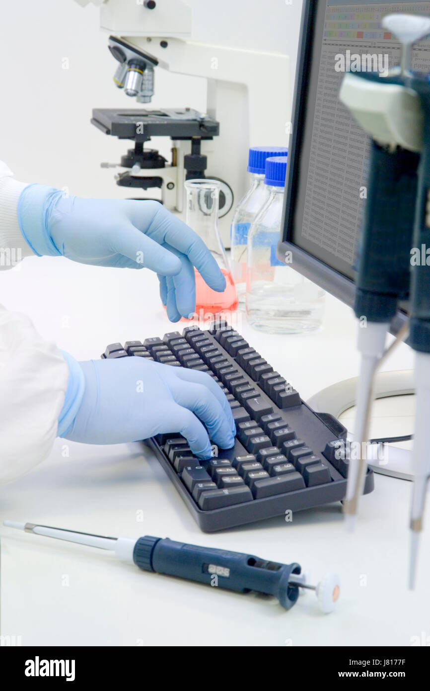 Gloved hands of a white-coated scientist using a computer in a bio-science laboratory Stock Photo