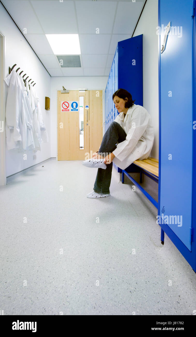A woman scientist puts on overshoes in the locker room before entering a sterile laboratory. Stock Photo